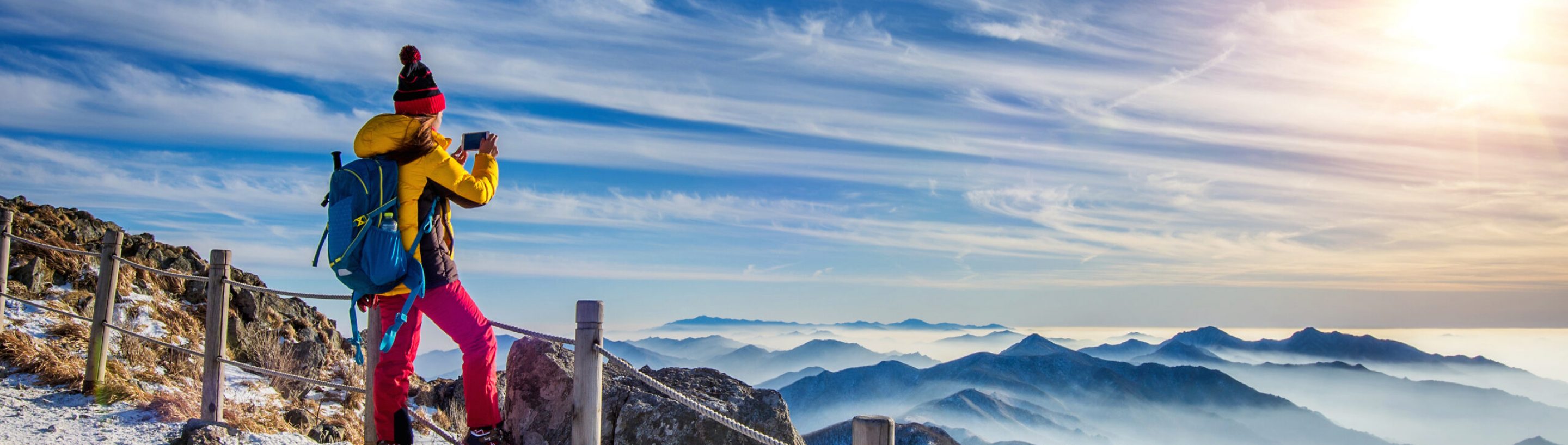 Young woman hiker taking photo with smartphone on mountains peak in winter.
